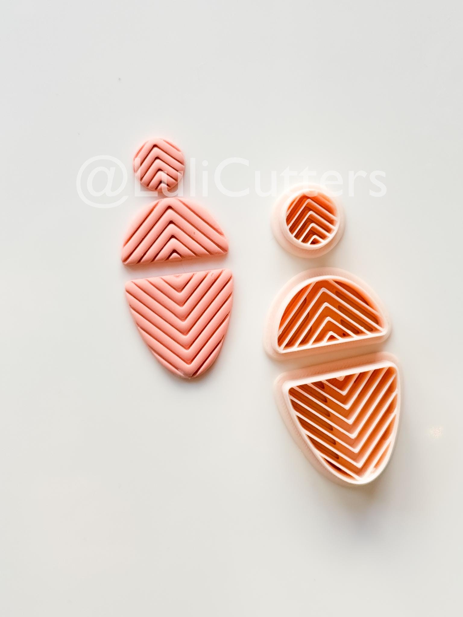 May include: Pink polymer clay cutters in various geometric shapes, including a circle, a half-circle, and two abstract shapes with chevron patterns. The cutters are arranged on a white surface.